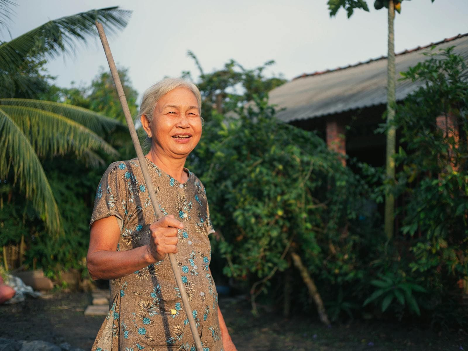 หญิงสูงอายุชาวไทยยิ้มแย้มในสวนหน้าบ้านในชนบท